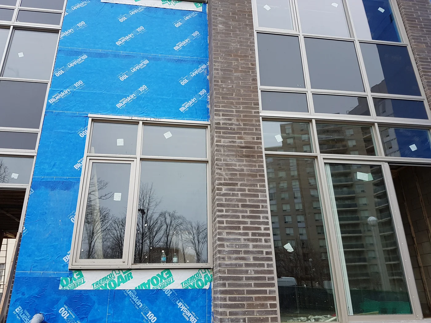 Blue air barrier membrane and transition membranes around windows beside brick masonry
